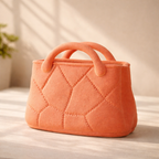 Orange quilted handbag on a light surface with a soft background