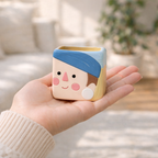 Hand holding a small square container with cartoon face design, blurred indoor background
