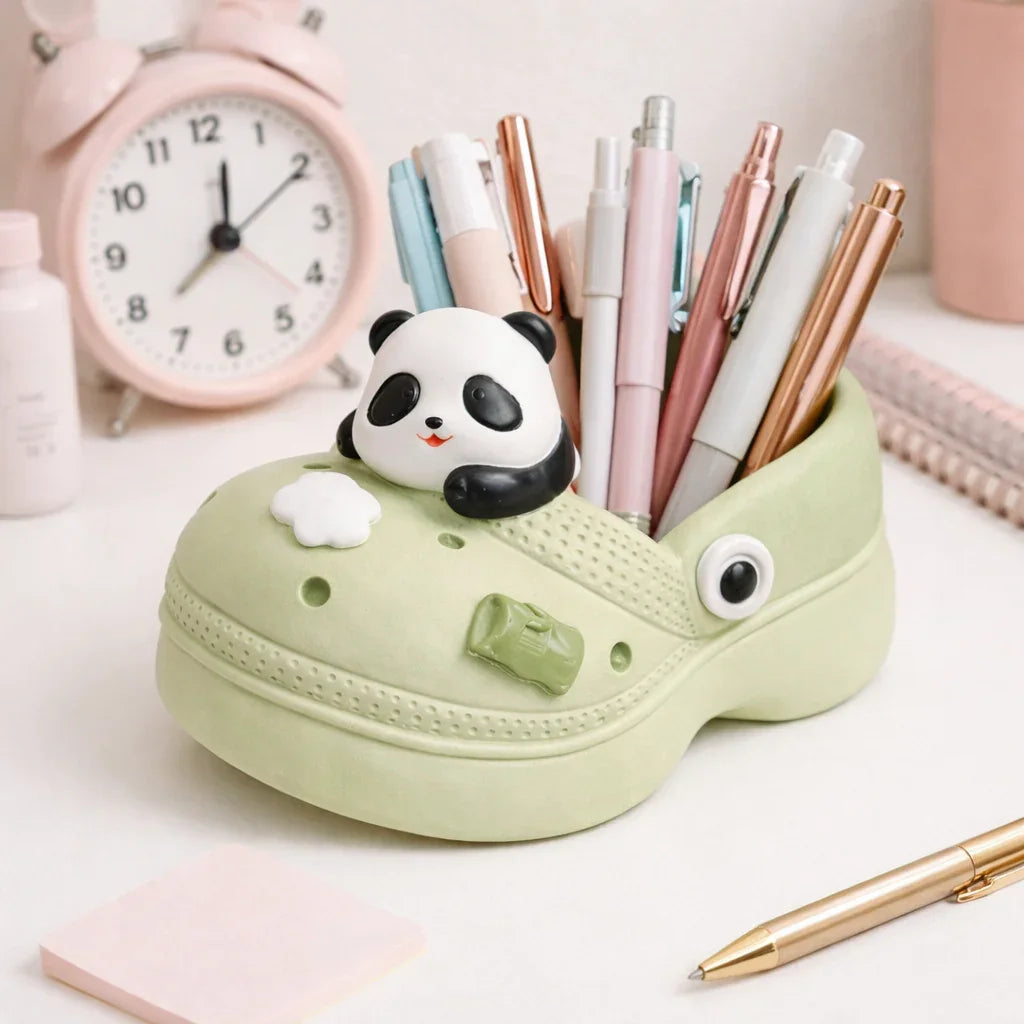 Cute panda pen holder shaped like a green shoe, filled with pens on a tidy desk near clock.