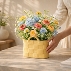 Hand holding a yellow woven basket with a colorful flower arrangement on a wooden table.