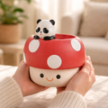 Cute ceramic mushroom-shaped container with a panda figurine on top, held by a person in a cozy indoor setting.