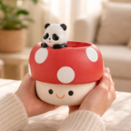 Cute ceramic mushroom-shaped container with a panda figurine on top, held by a person in a cozy indoor setting.
