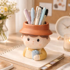 Cute boy-shaped ceramic pen holder with pens, on a desk with flowers and a notebook, Germiant