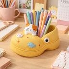Cute yellow shoe-shaped pen holder with cat and fish designs on a tidy desk, Germiant