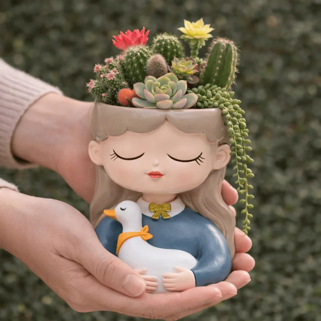 Ceramic planter shaped like a girl holding a duck with succulents and cacti on her head.