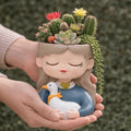 Ceramic planter shaped like a girl holding a duck with succulents and cacti on her head.
