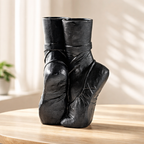Black ceramic vase shaped like a pair of ballet shoes on a wooden surface.