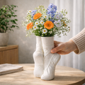 Hand holding a vase made from white socks filled with colorful flowers on a wooden surface.